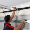 Homeowner inspecting garage door roller for cracks and wear damage during routine maintenance