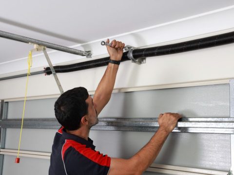 Homeowner inspecting garage door roller for cracks and wear damage during routine maintenance