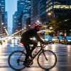 Urban cyclist wearing a well-fitted modern helmet with integrated rear light riding through busy city traffic at dusk