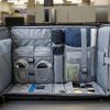 A TSA approved travel backpack laid flat and open at an airport security checkpoint, showing a dedicated laptop compartment and organized interior pockets