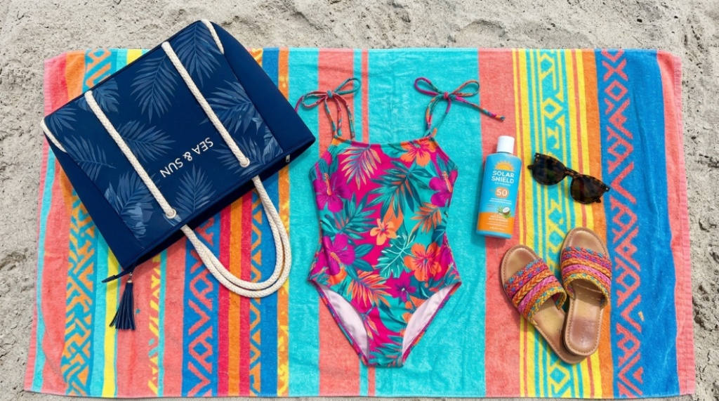 Flat lay of a stylish neoprene swim tote next to a colourful swimsuit, sunscreen, and sandals on a summer towel