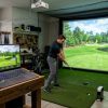 A gaming laptop with RTX graphics displaying a lush golf course on a golf simulator setup in a home garage