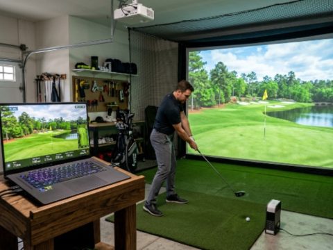 A gaming laptop with RTX graphics displaying a lush golf course on a golf simulator setup in a home garage
