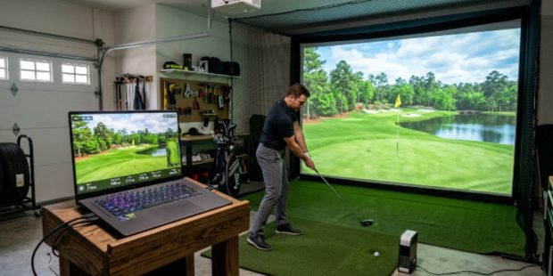 A gaming laptop with RTX graphics displaying a lush golf course on a golf simulator setup in a home garage
