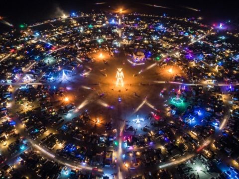 Aerial view of Black Rock City circular street grid in Nevada's Black Rock Desert at night with art installations lit up during Burning Man 2026