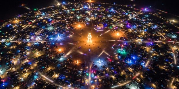 Aerial view of Black Rock City circular street grid in Nevada's Black Rock Desert at night with art installations lit up during Burning Man 2026