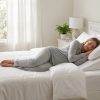 Person sleeping comfortably in naturally lit minimalist bedroom under white linen sheets.